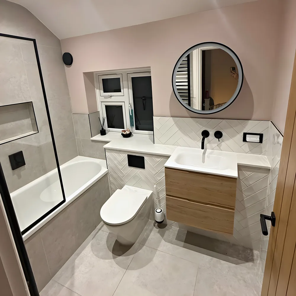 A bathroom with baby pink walls, a round black mirror, an oak vanity unit and a wall hung toilet