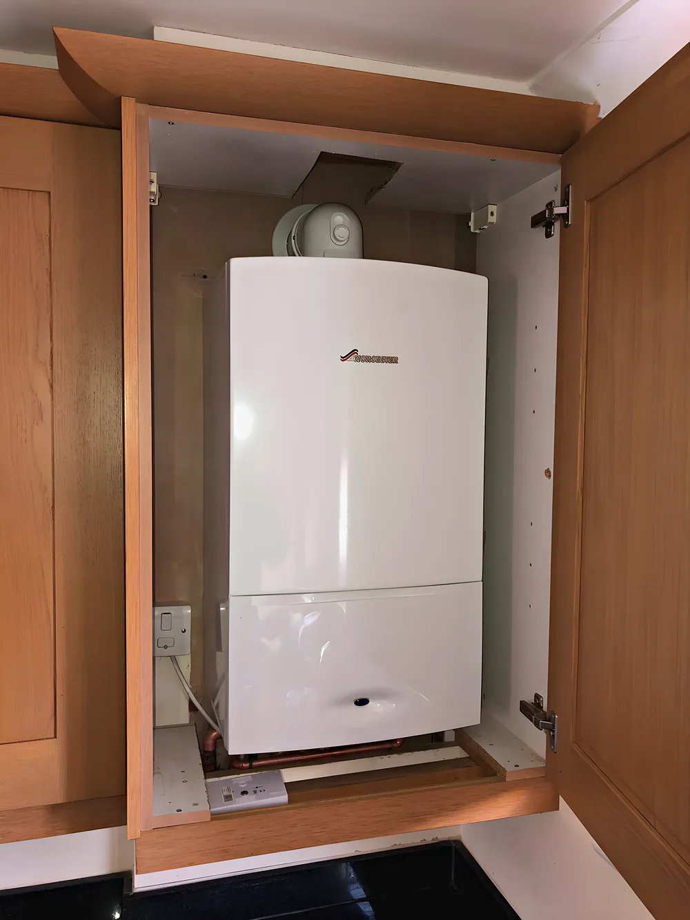 A new white combi boiler fitted neatly inside an oak kitchen cupboard