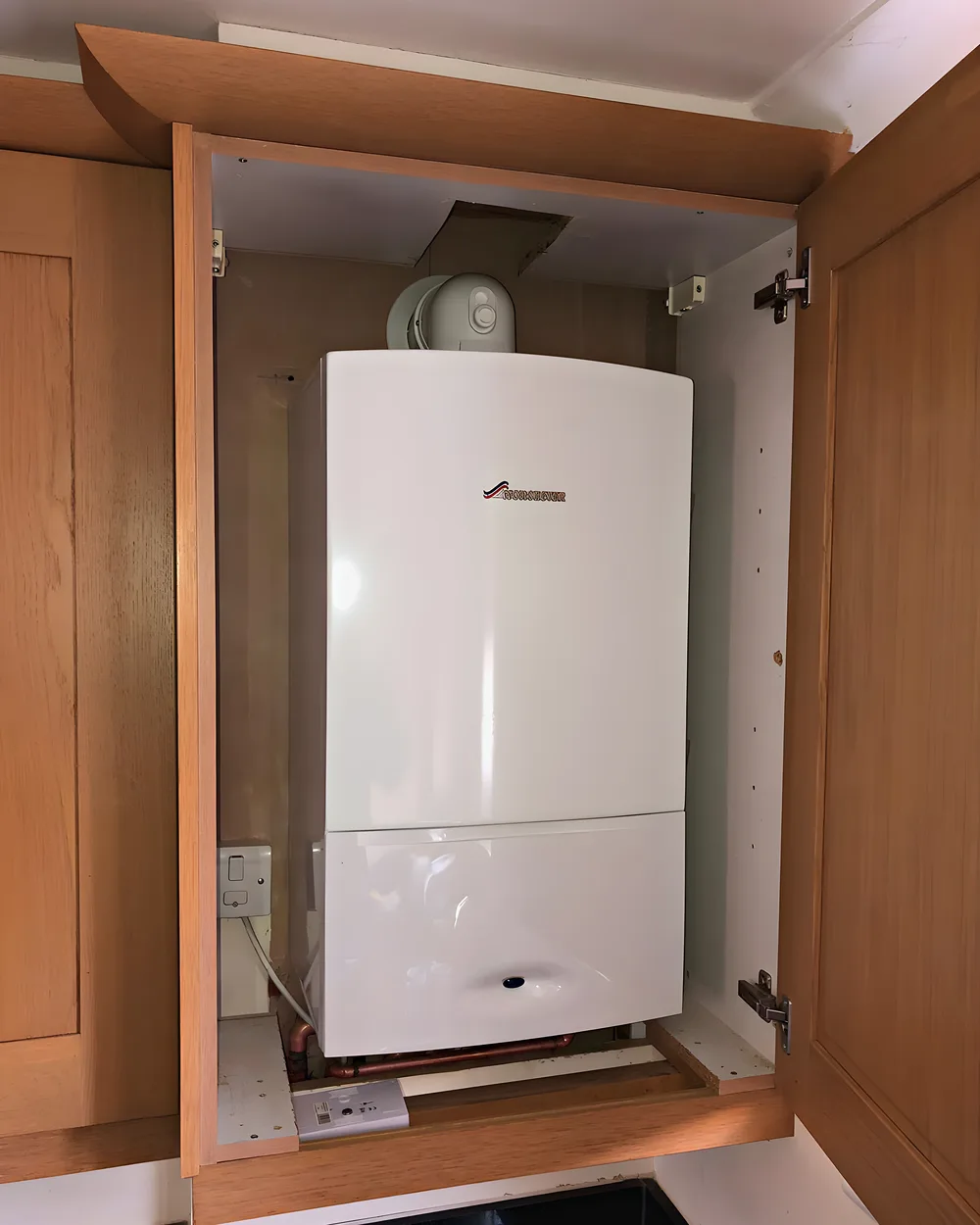 A new white combi boiler fitted neatly inside an oak kitchen cupboard
