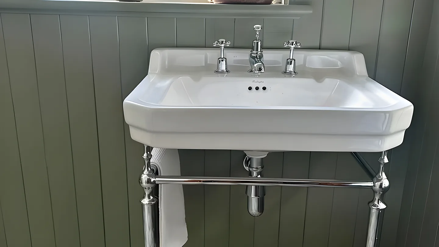 A cloakroom with sage green panelling, a washstand basin on chrome legs and a patterned tiled floor