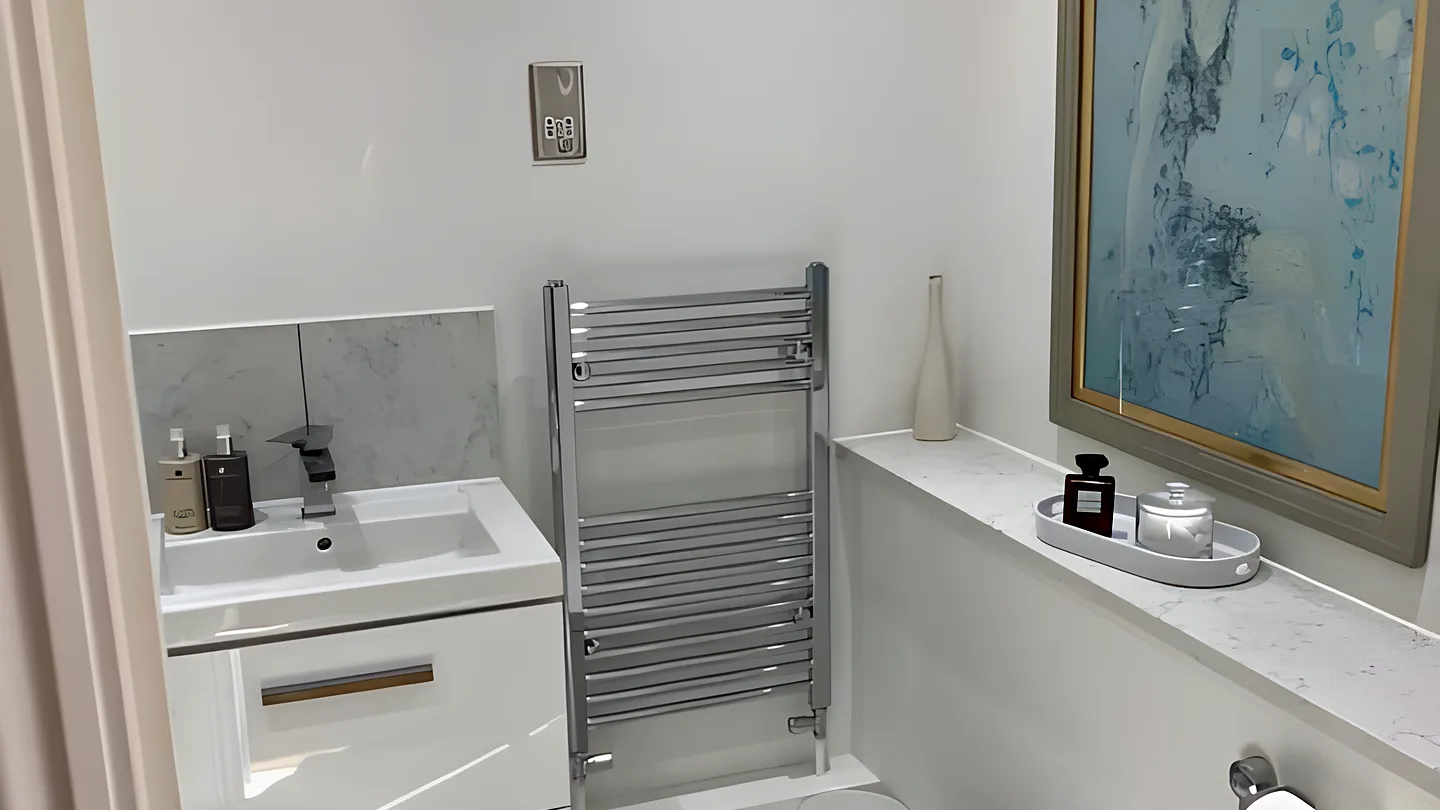 A white cloakroom with a vanity unit, chrome towel rail and a framed painting