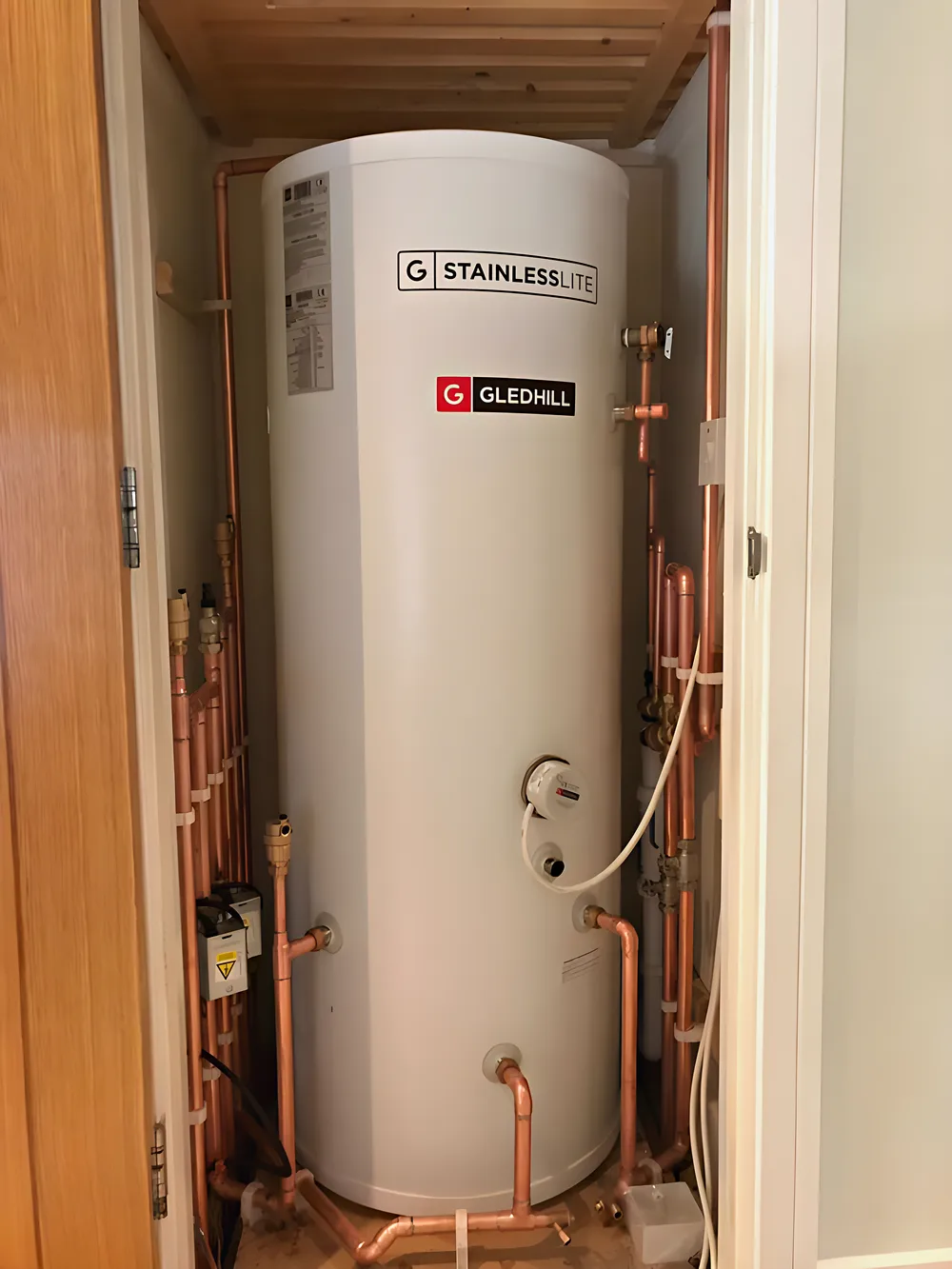 A stainless unvented hot water cylinder in a cupboard with copper pipework
