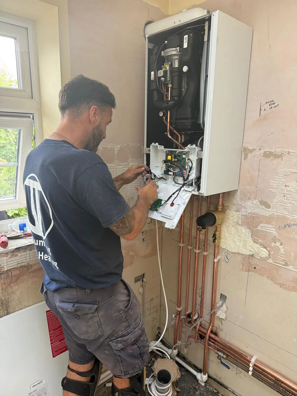 A JT Plumbing & Heating engineer working on a wall hung boiler with its front cover off
