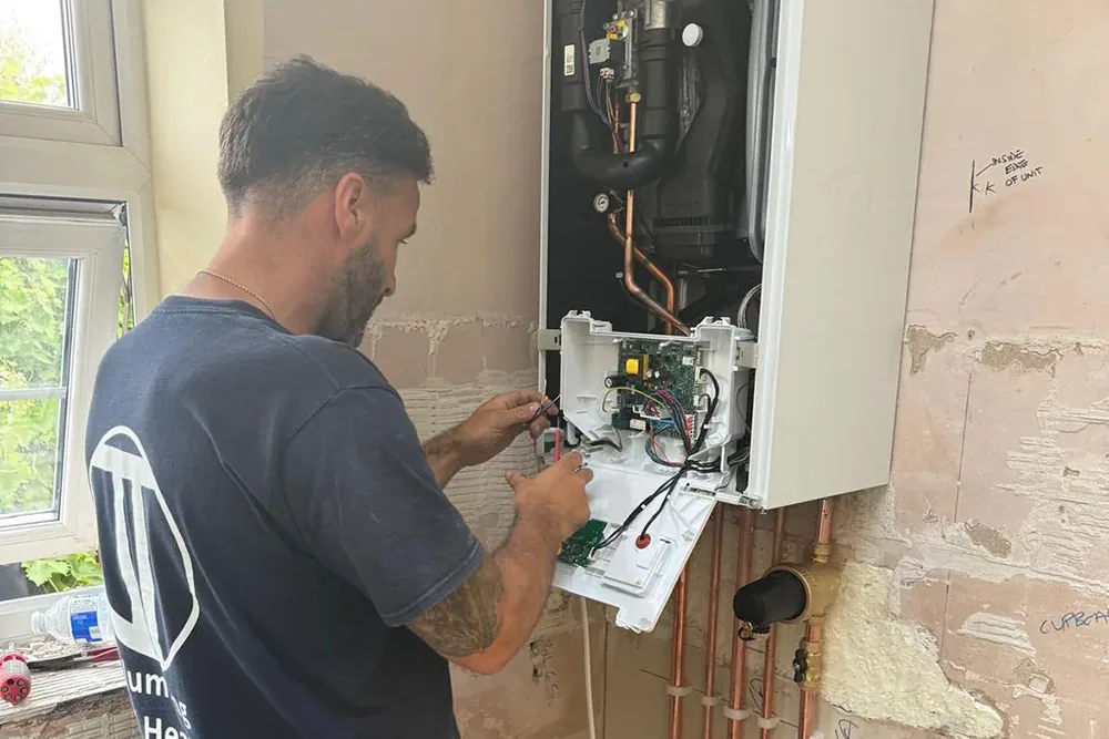 A JT Plumbing & Heating engineer working on a wall hung boiler with its front cover off