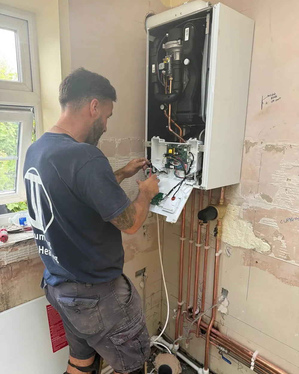 A JT Plumbing & Heating engineer working on a wall hung boiler with its front cover off