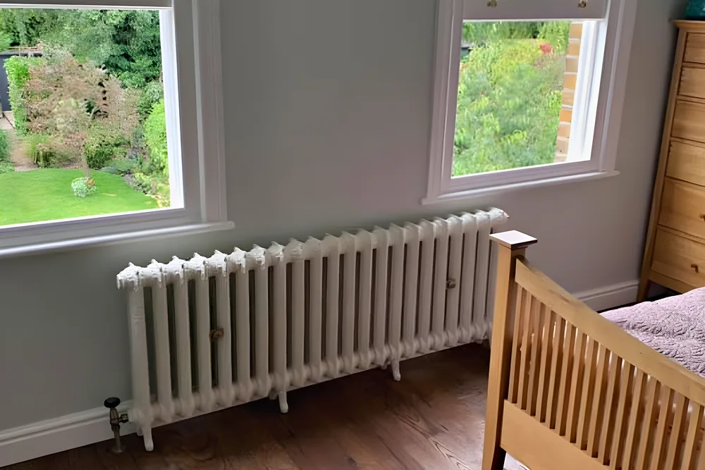 A white column radiator in a bedroom with an oak floor and garden views