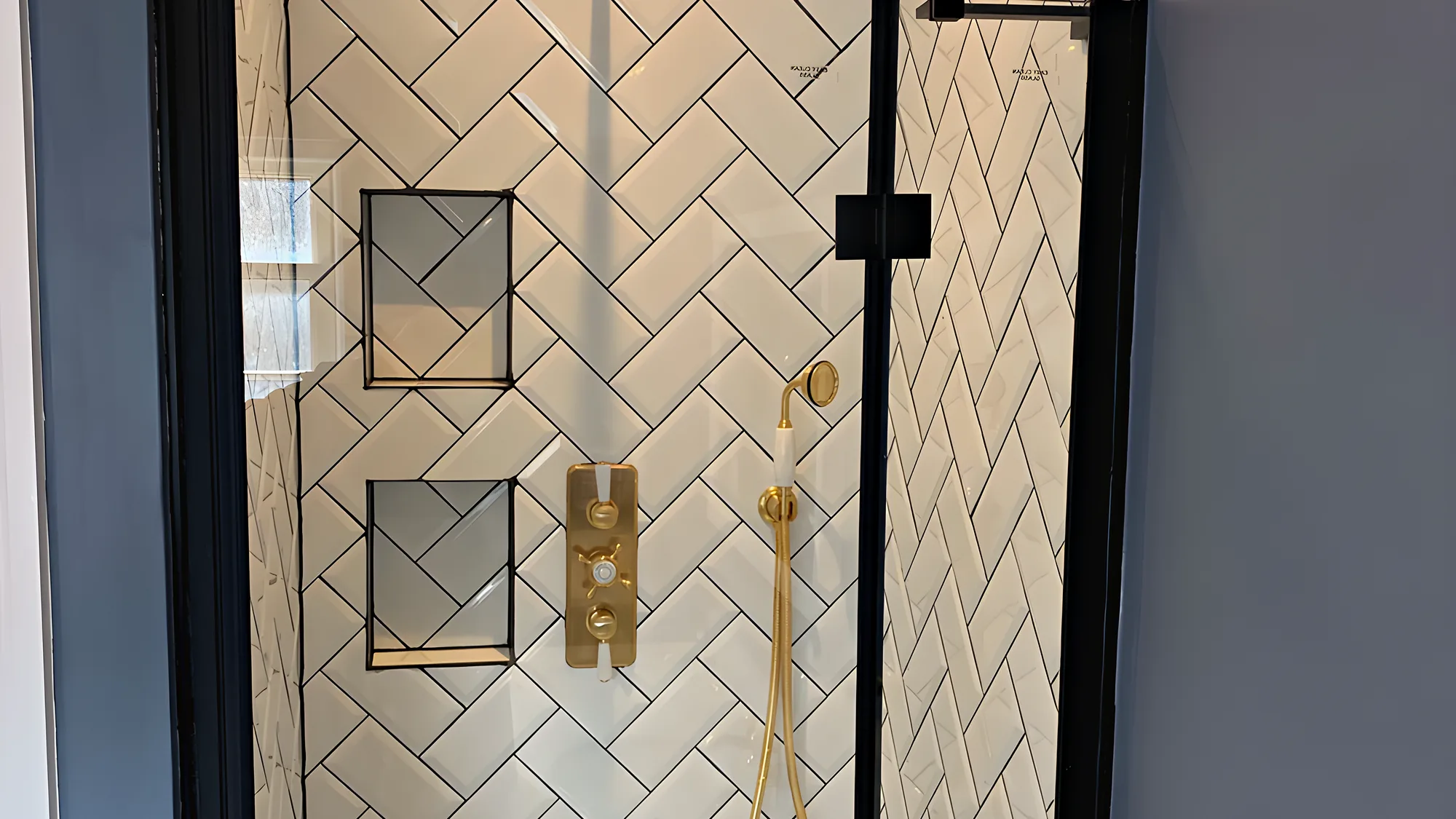 A walk in shower with white herringbone tiles, two niches and a brushed brass rain shower