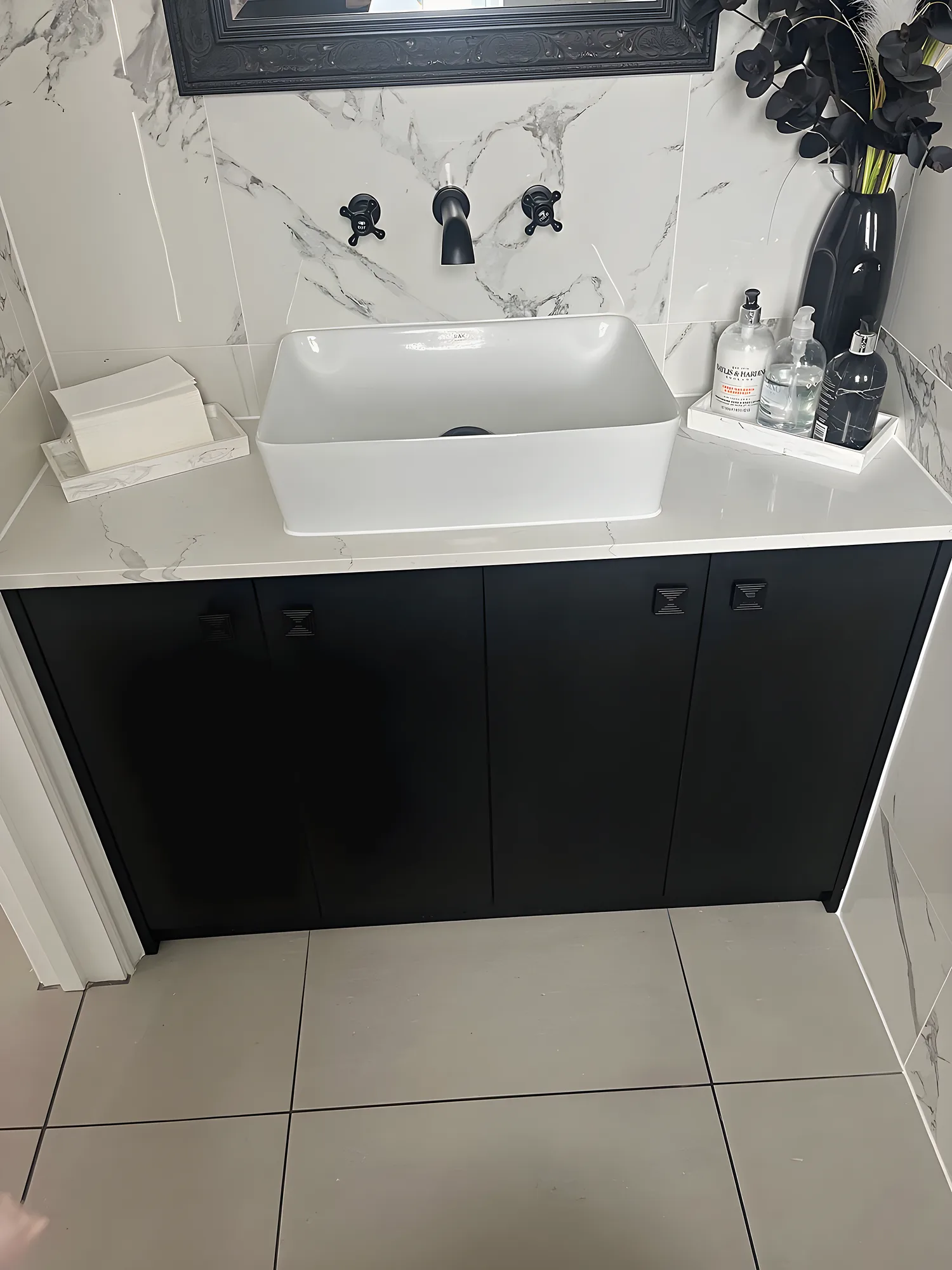 A white vessel basin on a black vanity unit with marble effect tiles