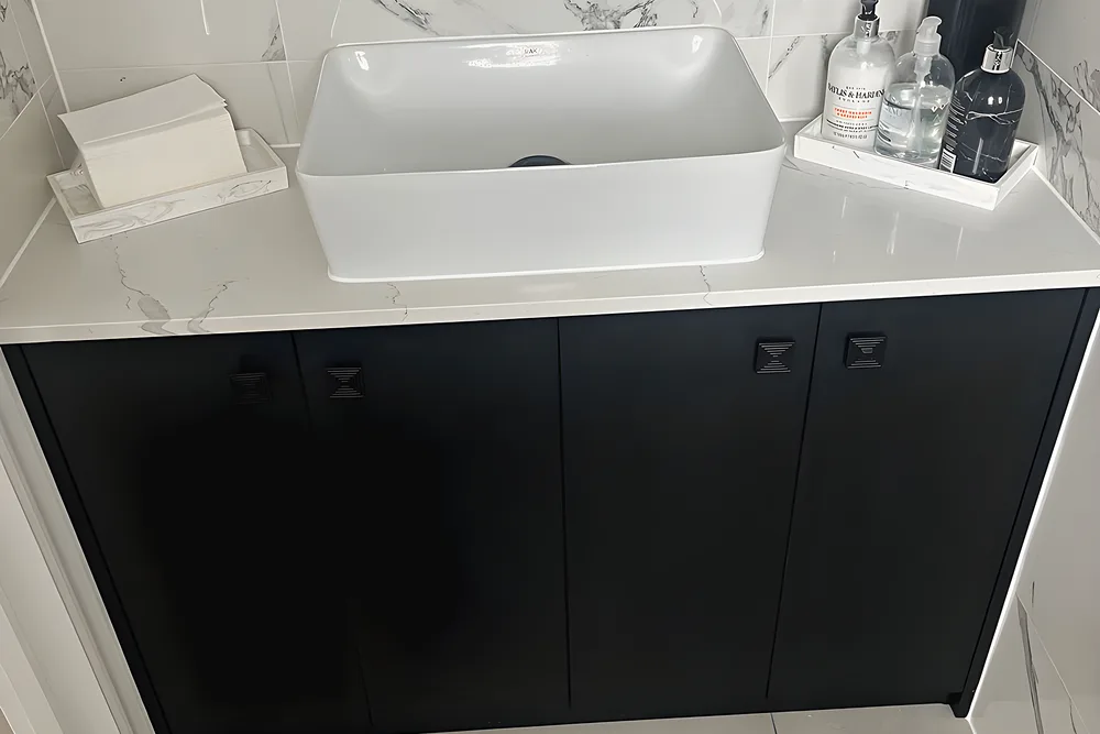 A white vessel basin on a black vanity unit with marble effect tiles